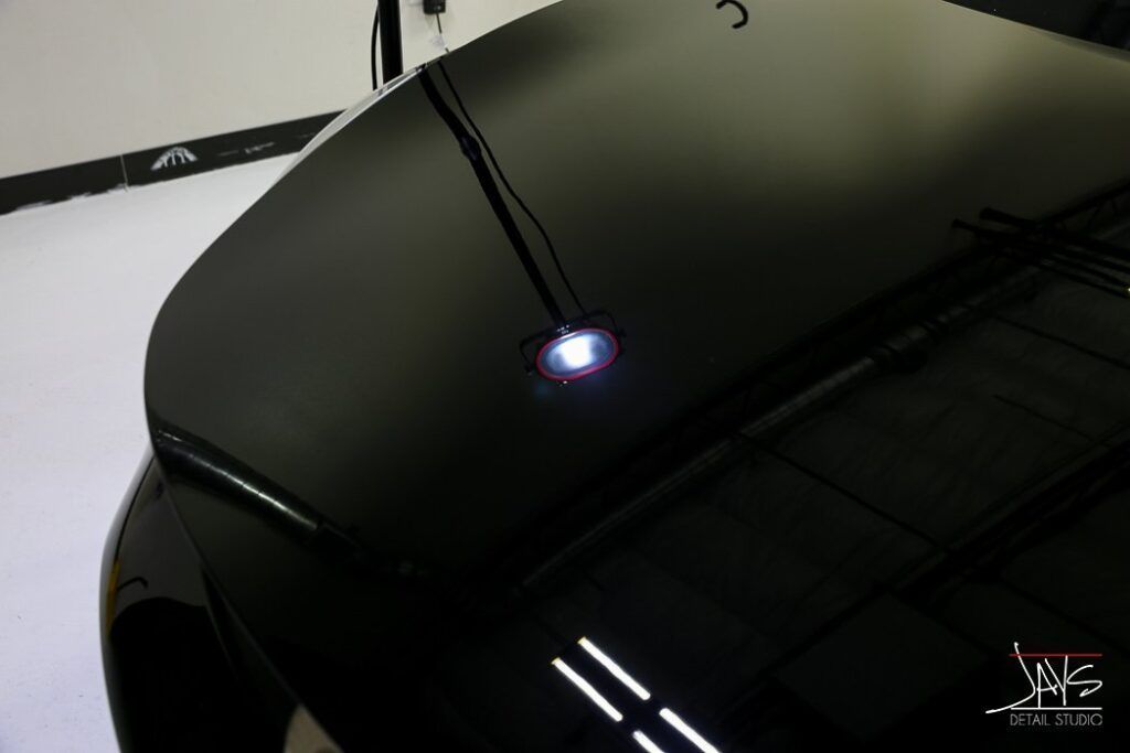 Black car hood reflecting light with a bright spot, highlighting the shiny surface in a studio setting.