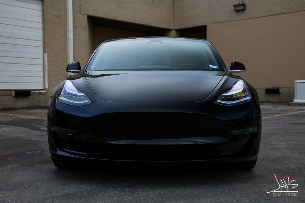 Black Tesla Model 3 electric car parked in front of a tan building.