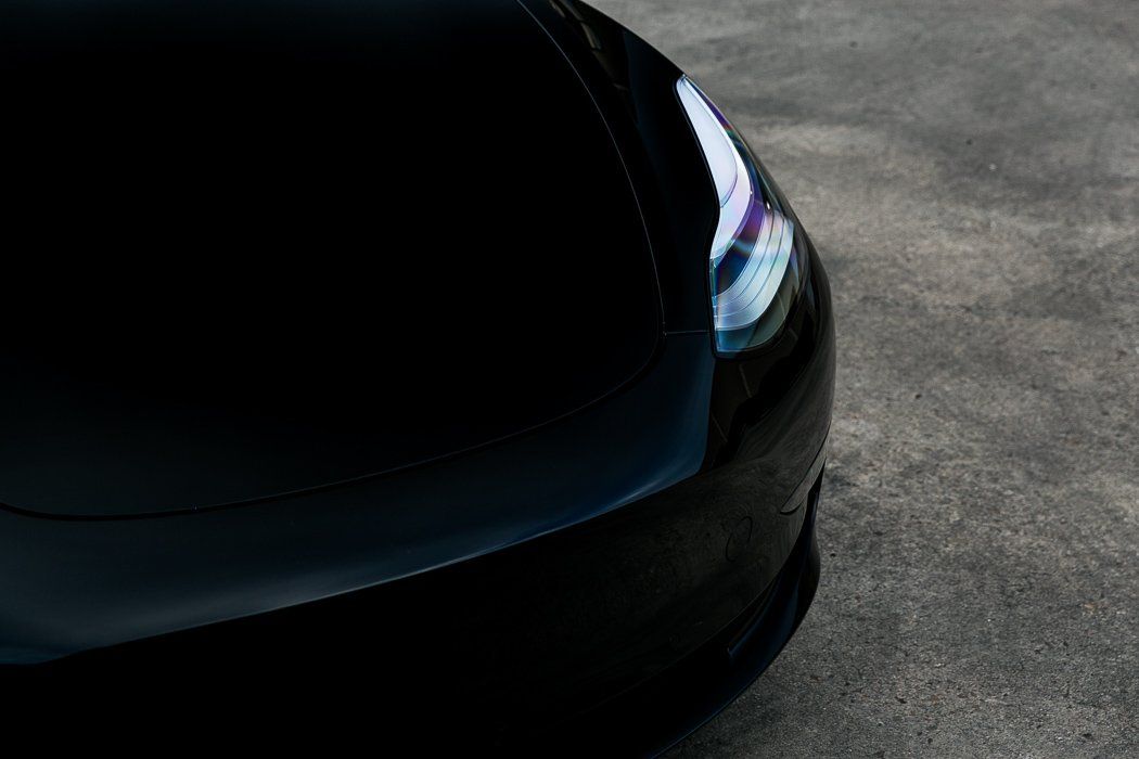 Black car's front end, reflecting light on a concrete surface.