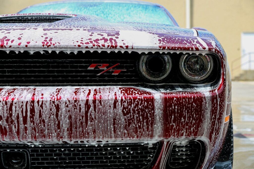 Red Dodge Challenger with foam covering the front, being washed.