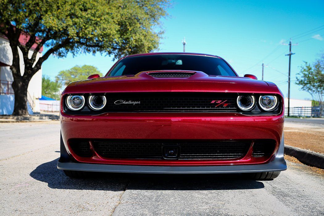 Red Dodge Challenger, front view, parked on a street with a tree and building in the background.