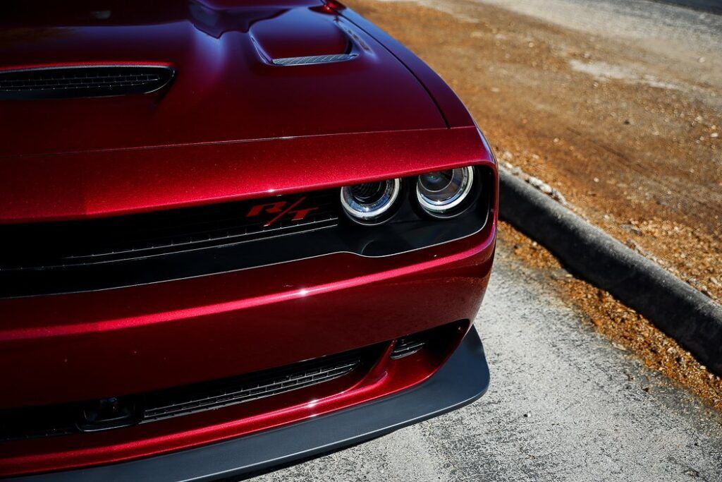 Red Dodge Challenger car, front view, parked on a road in sunlight.