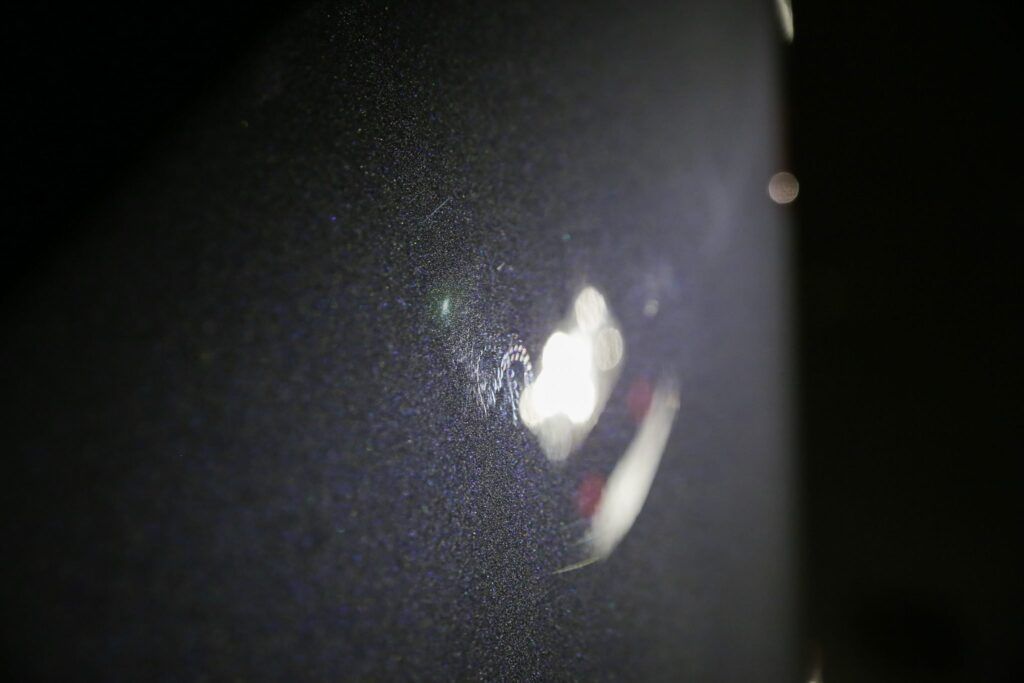 Close-up of a dark textured surface reflecting a bright light and a distorted red and white shape.