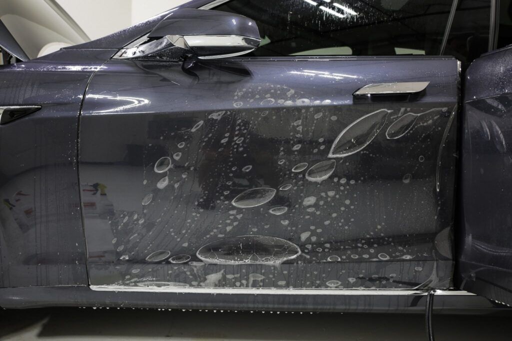 Car door covered in soap, being washed. Dark blue car in a garage.