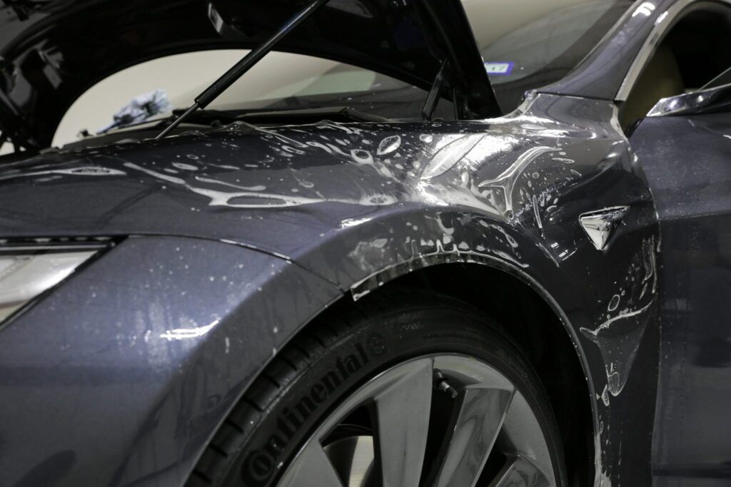 Dark grey car fender being wrapped with protective film.