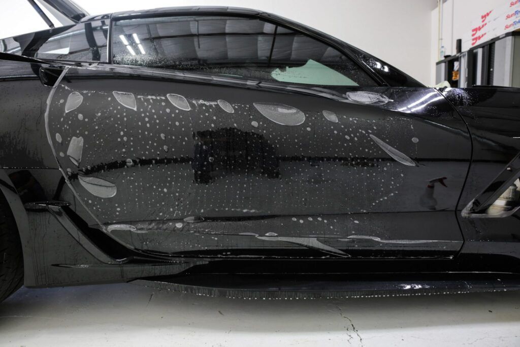Black car with paint protection film applied, showing bubbles and water.