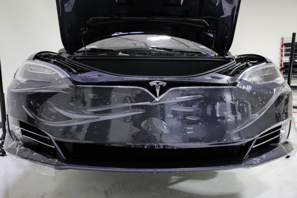 Black Tesla car with the hood open, undergoing paint protection film installation in a shop.