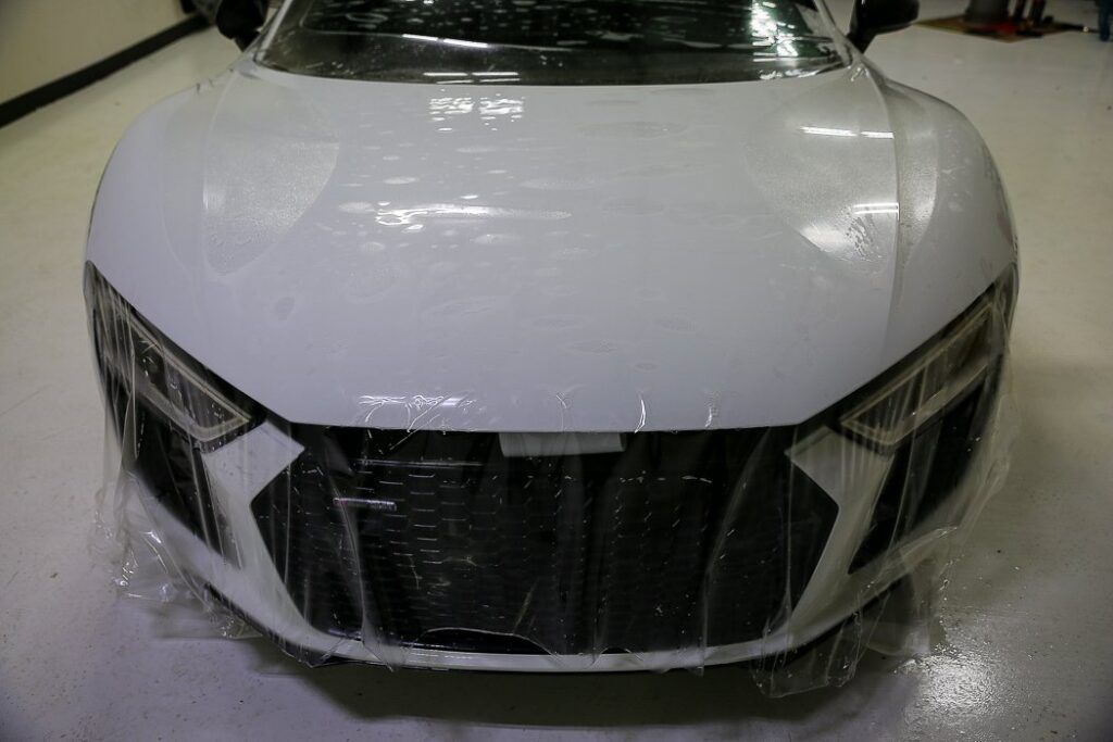 White sports car being covered in protective plastic wrap in a garage.