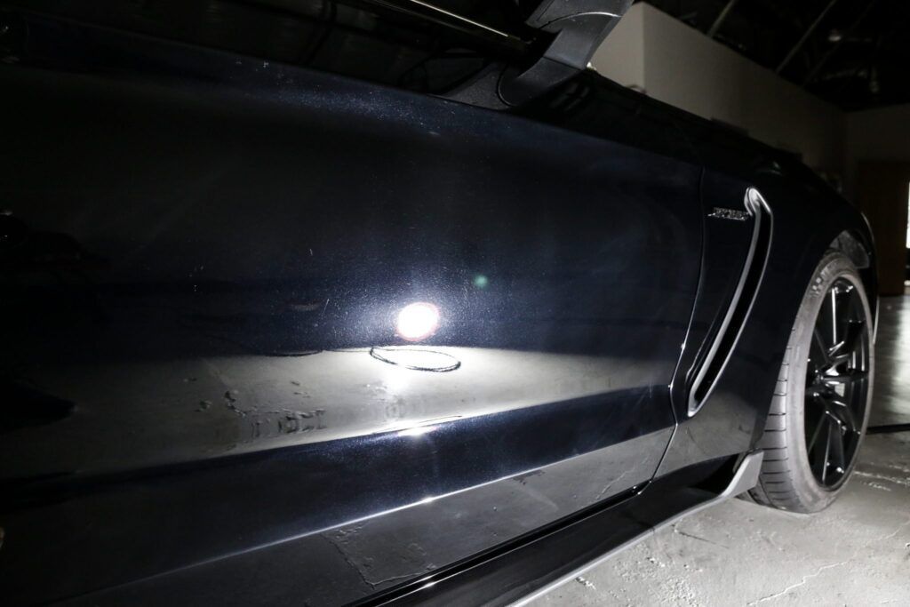 Black sports car side, door ajar, black tire, dark interior.