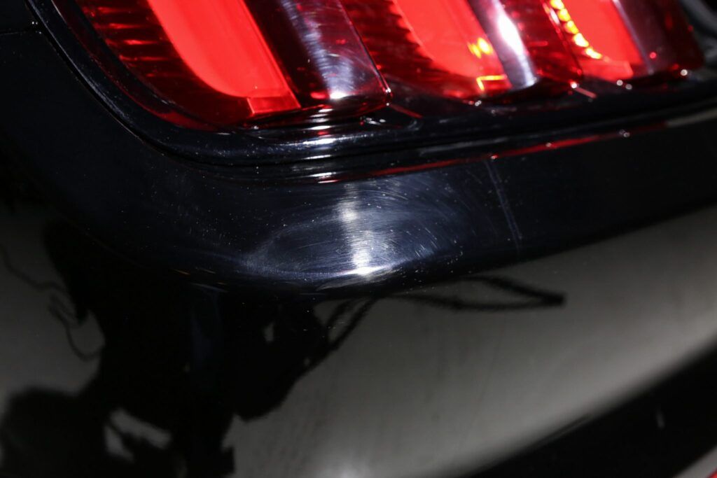 Close-up of a black car's taillight and bumper, reflecting light.