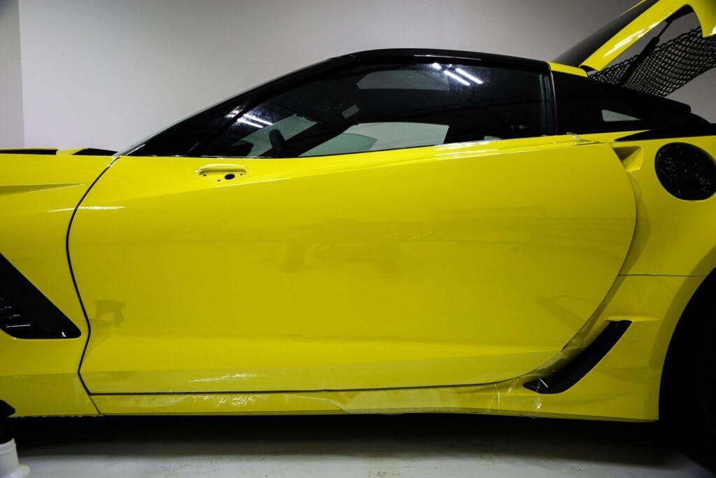 Yellow sports car parked indoors, side view, doors closed, black trim.