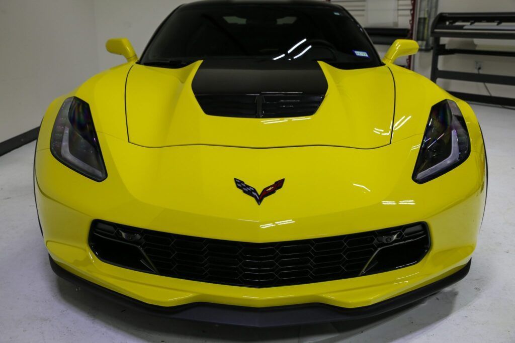 Yellow Corvette sports car, front view, black accents, interior lighting.