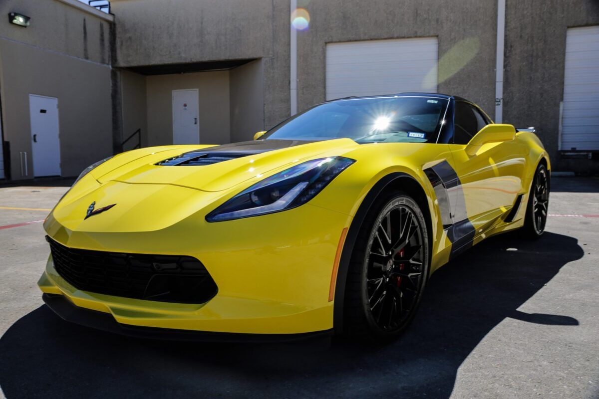 Yellow Corvette sports car with black accents, parked in front of a building on a sunny day.