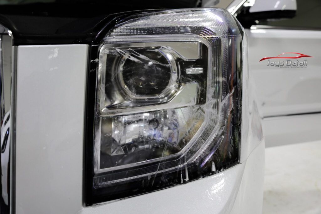 Close-up of a car's headlight on a white vehicle, showing detail of the lens and surrounding chrome trim.