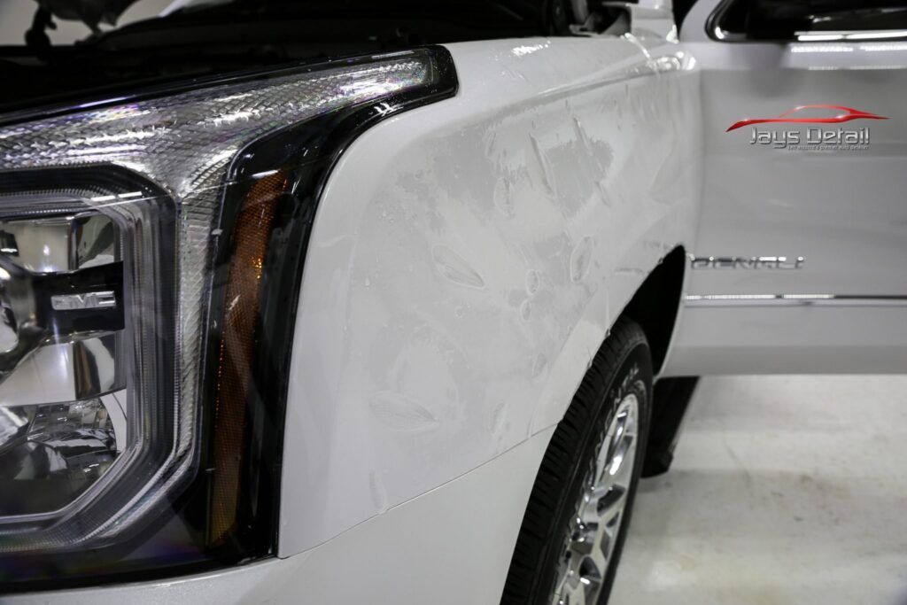 White GMC Yukon SUV, close-up of the front left side, with visible headlights and the door slightly open.