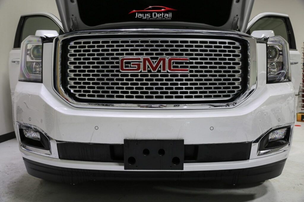 White GMC Yukon SUV, front view, hood open, showing the grill, and license plate holder.