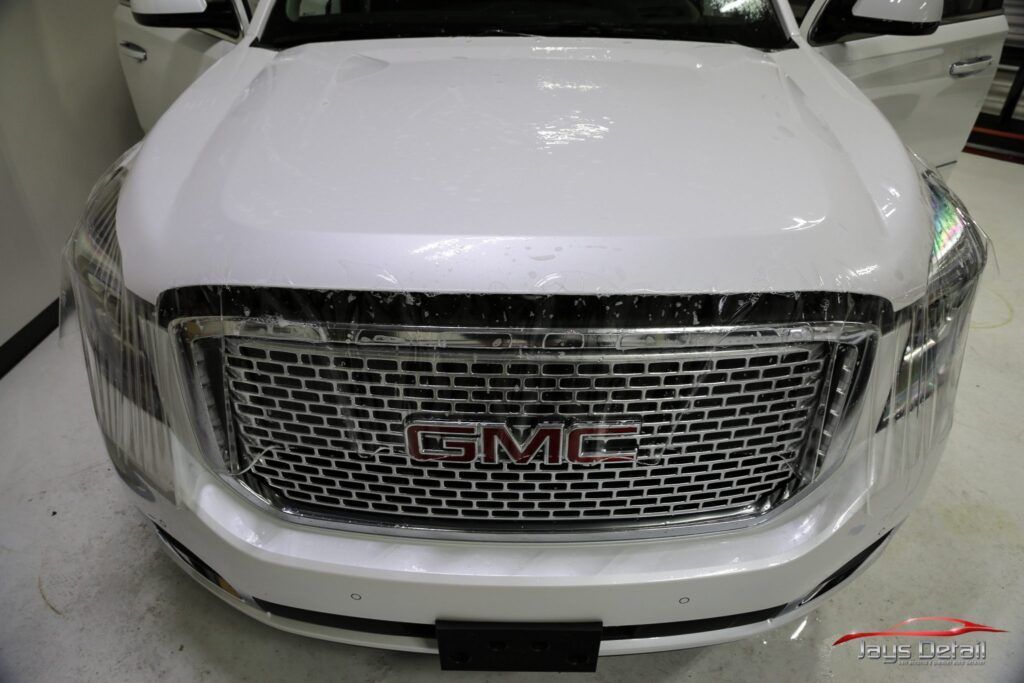 White GMC vehicle with protective film on the front, including the hood and grill.