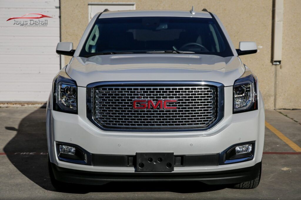 White GMC Yukon SUV, facing forward, parked. Shiny chrome grill, black front bumper, license plate area visible.