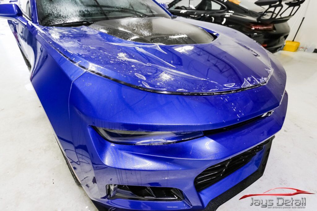 Blue sports car with protective film being applied in a detailing shop.
