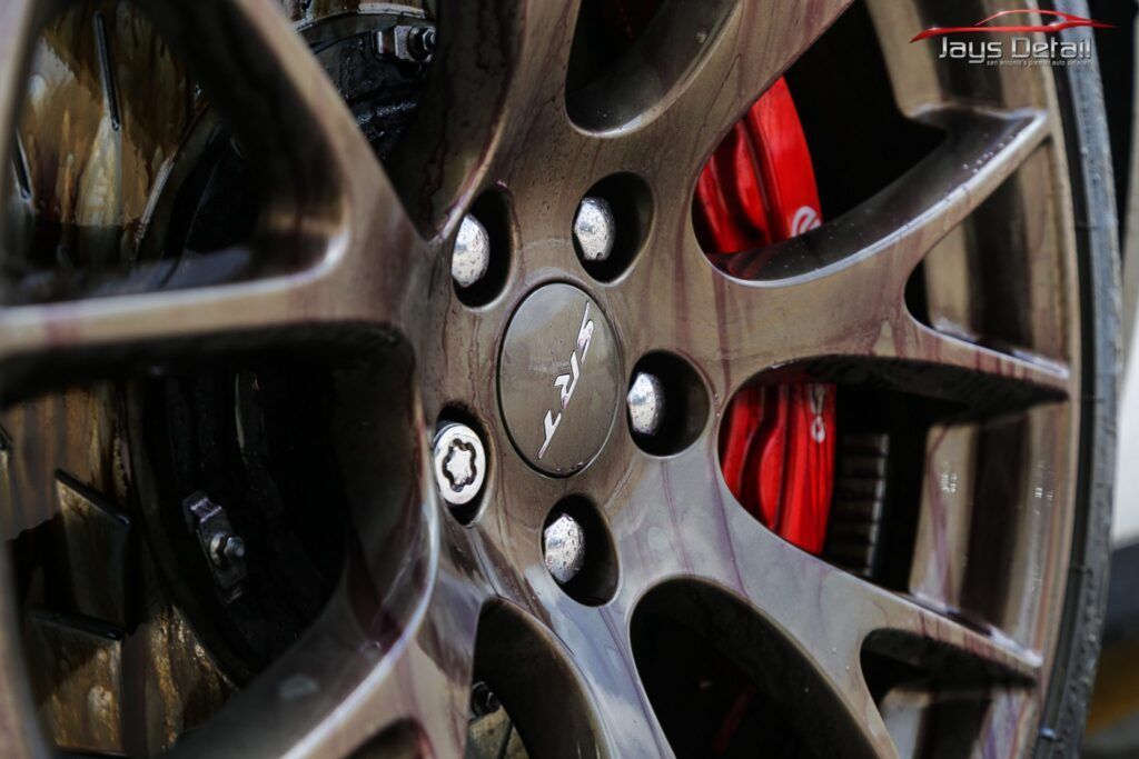 Close-up of a car wheel with a black rim, silver lug nuts, and a red brake caliper.