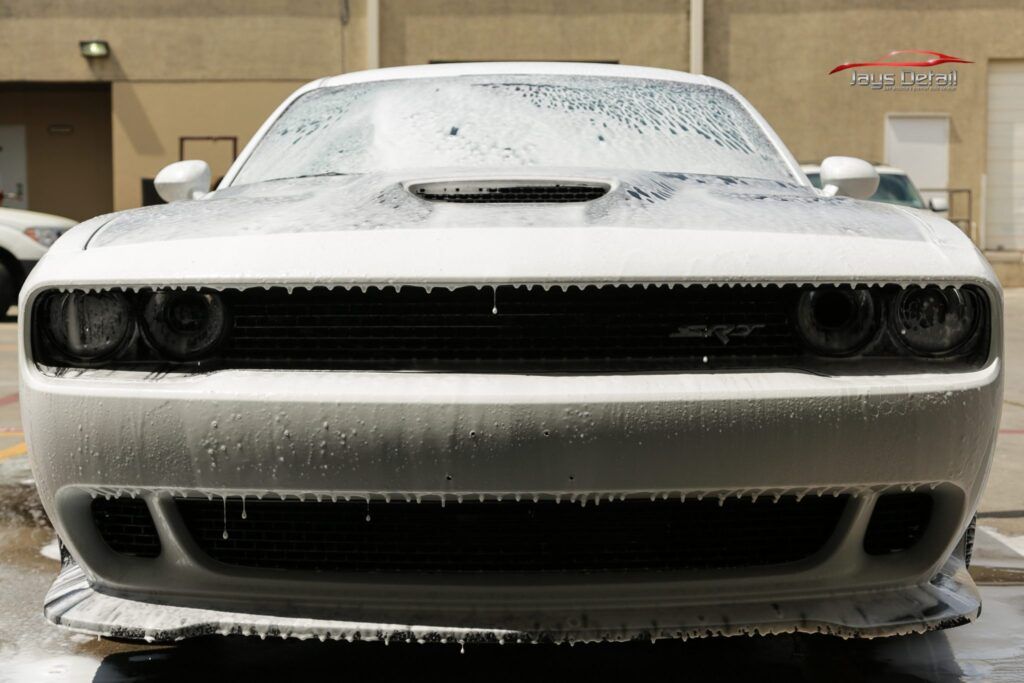 White Dodge Challenger covered in thick white foam at a car wash.