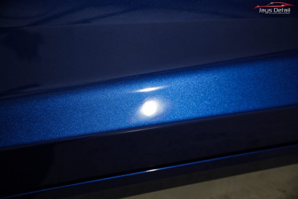 Close-up of a shiny blue car door with visible light reflection.