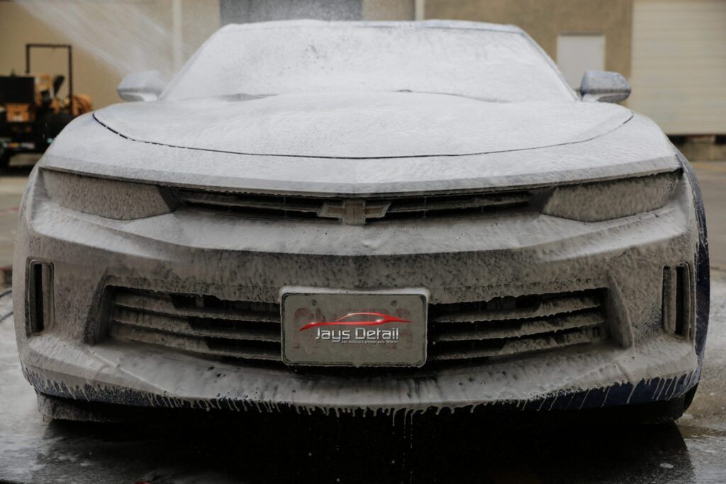 A gray Chevy Camaro covered in white foam, being washed at a car wash.
