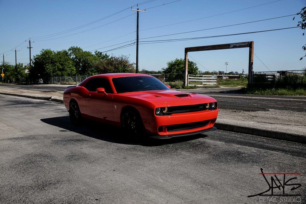 Red Dodge Challenger parked on a paved road on a sunny day.