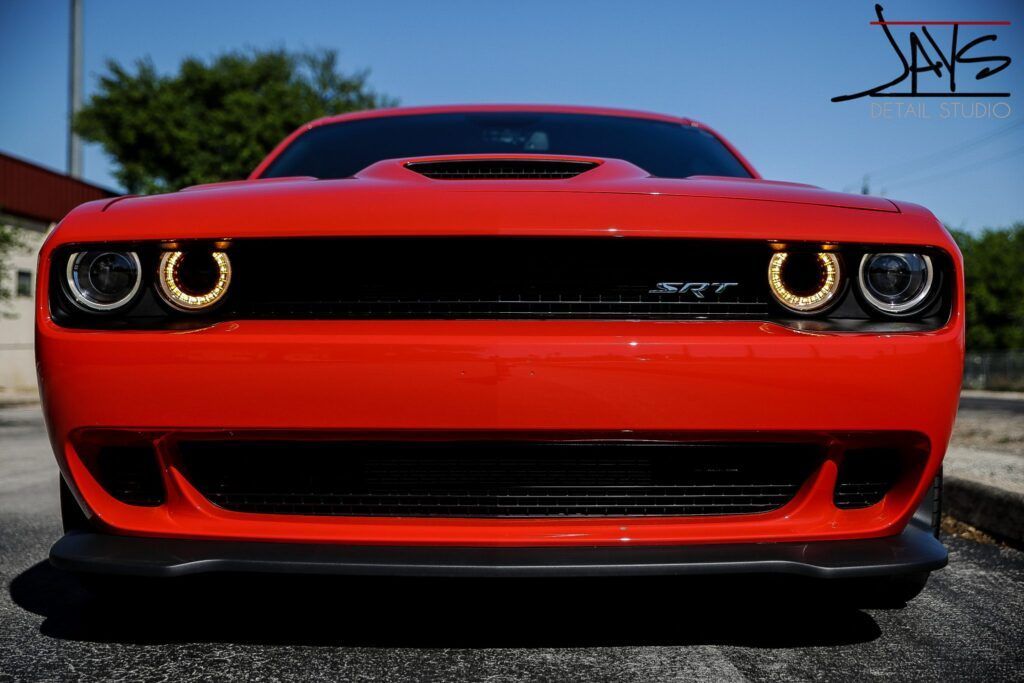 Red Dodge Challenger, front view, black accents, with golden halo headlights.