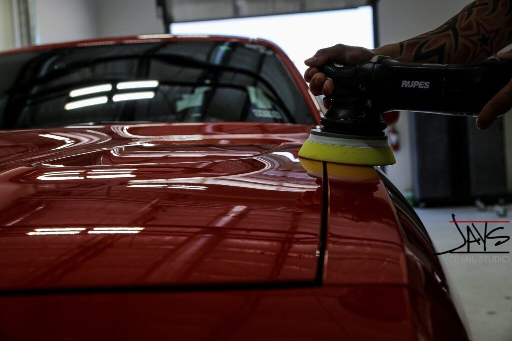 Person polishing red car hood with a buffer.