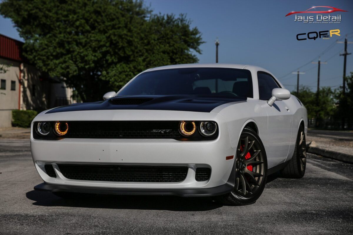 White Dodge Challenger with black hood, parked on a street with a building in the background.