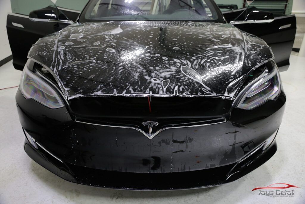 Black Tesla car with protective film applied to the hood and front bumper, indoors.