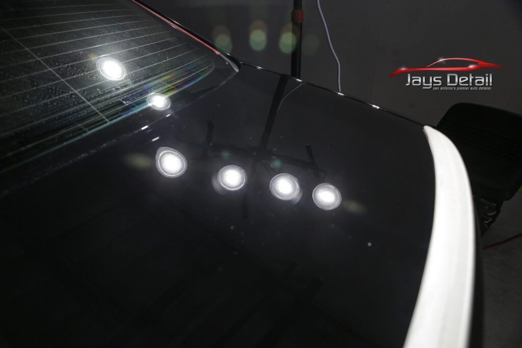 Black car's trunk with reflections of lights, showing polished surface.