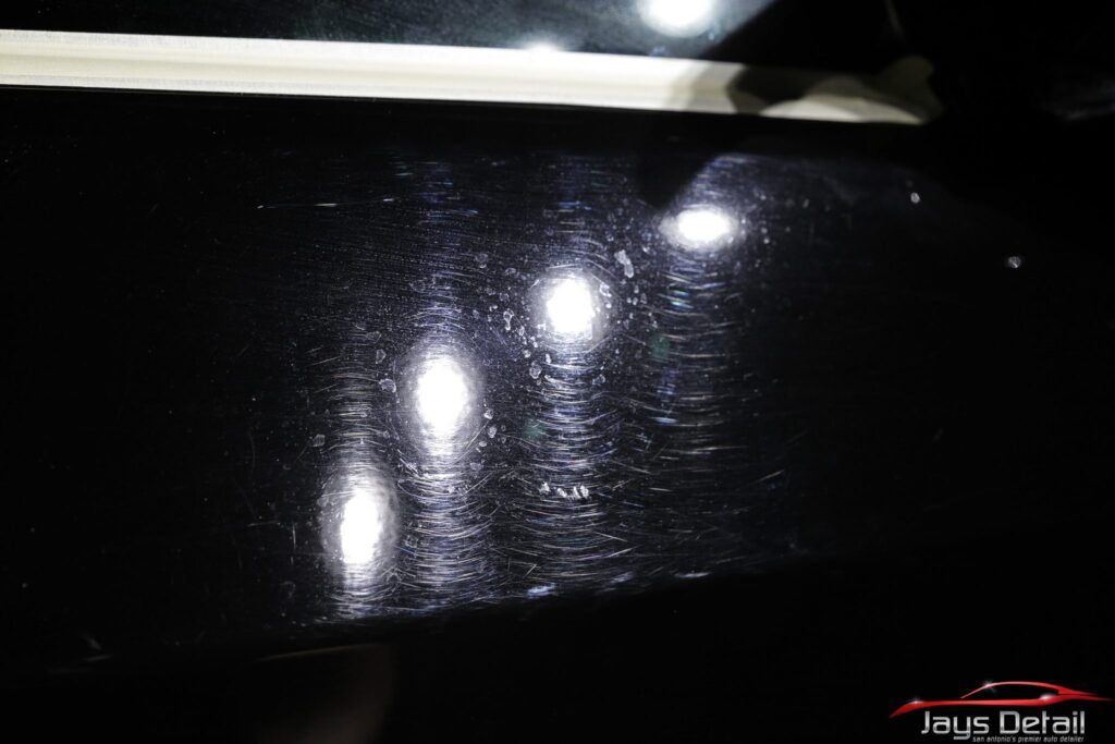 Close-up of black car paint with swirl marks and light reflections.