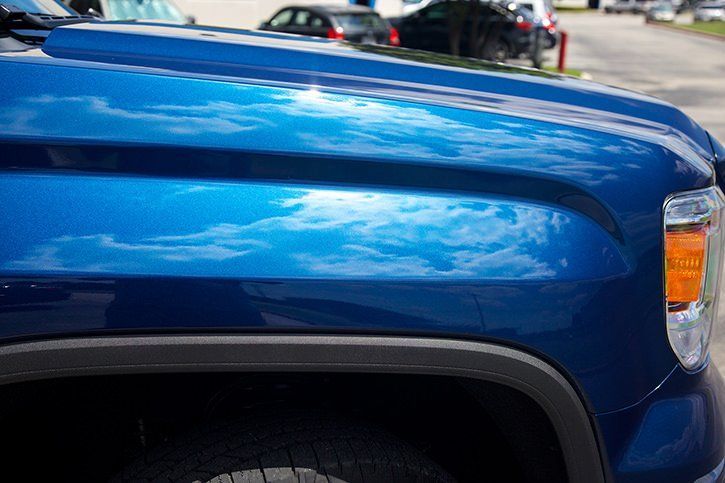 Blue pickup truck hood reflecting the sky and nearby vehicles.