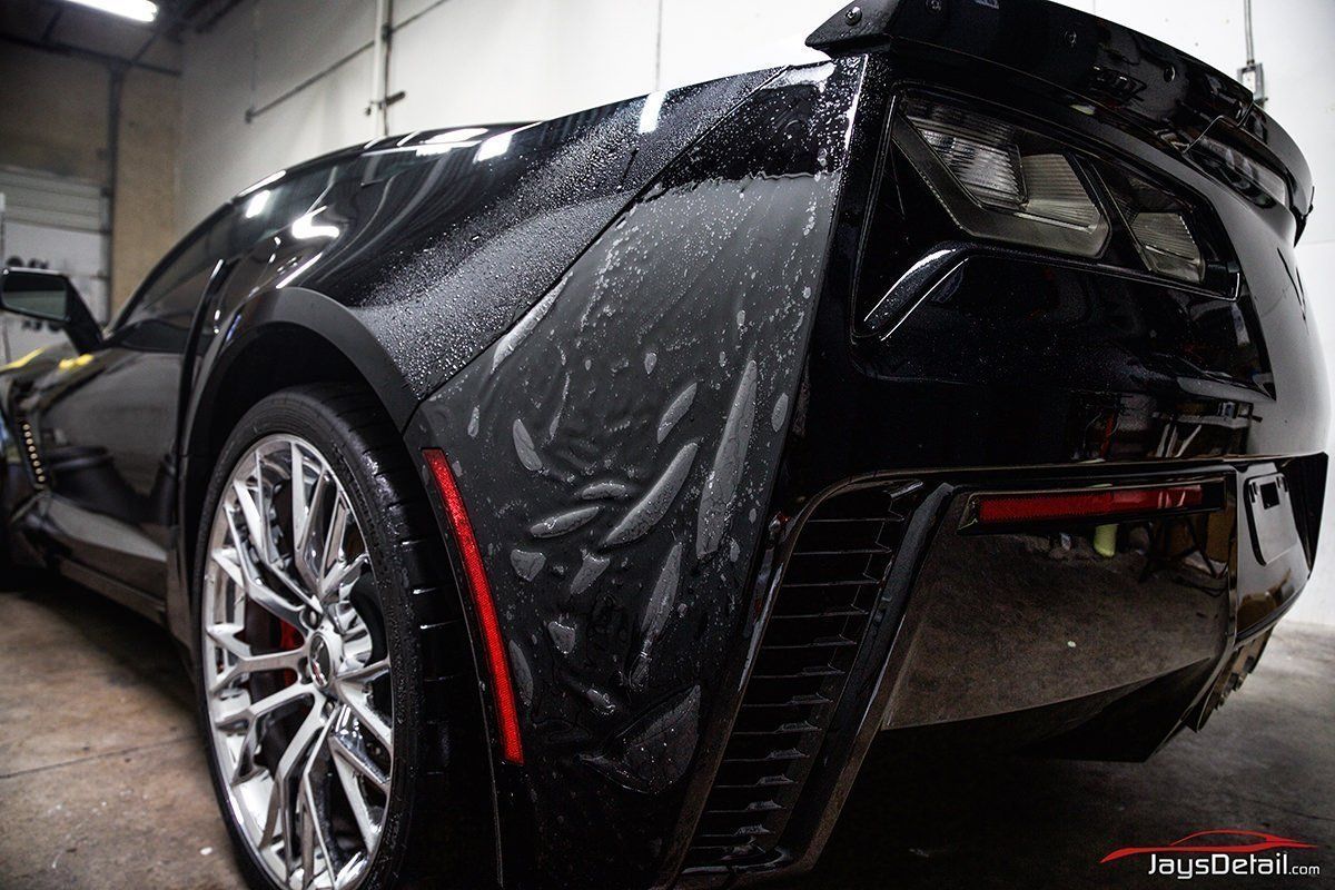 Black sports car with wet appearance, chrome wheels, and red taillights.