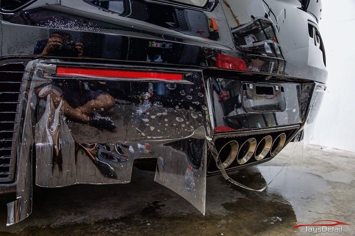 Rear view of a black sports car with four exhaust pipes and a wet, glossy finish.