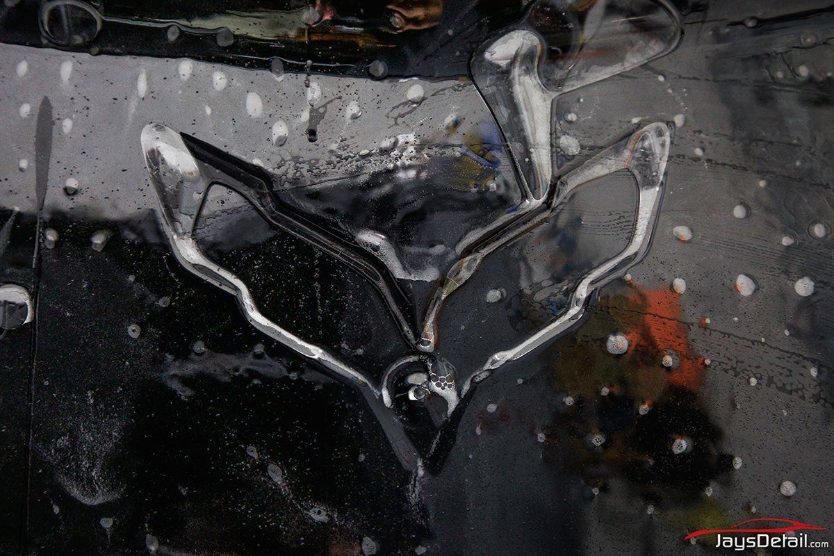 Chrome Corvette emblem on a wet, black car surface.