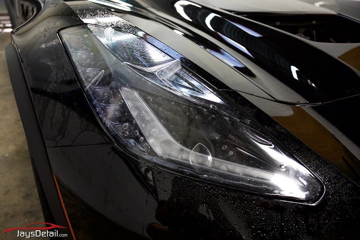 Black sports car headlight; close-up view, slightly wet, with visible internal details.