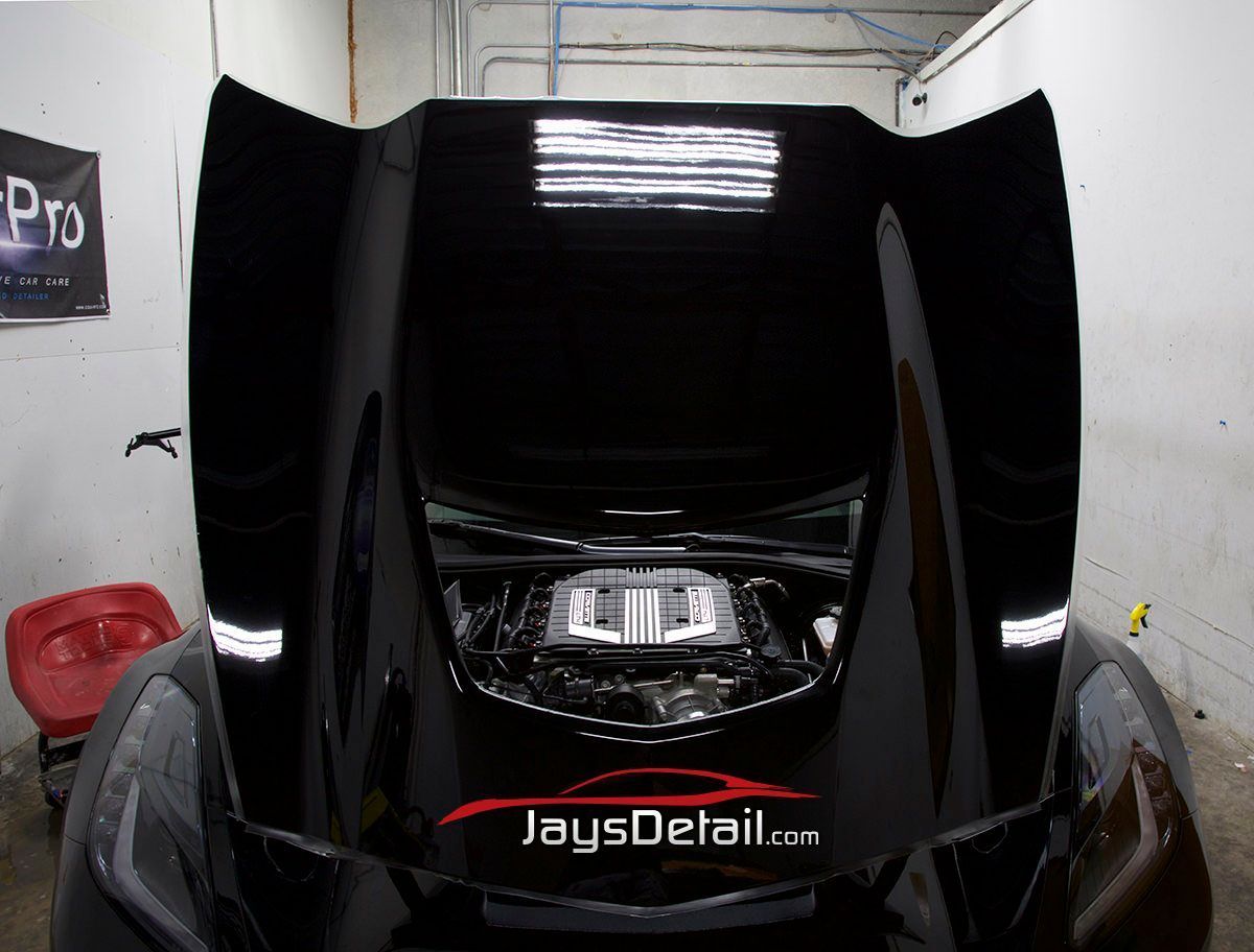 Black Corvette hood open, engine exposed. Jay's Detail shop, interior. Shiny black paint.