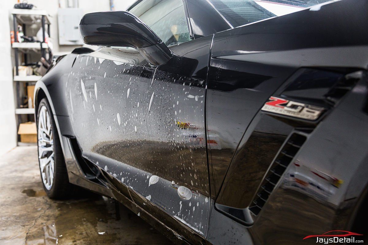 Black sports car with protective film applied, detail shot in a garage.
