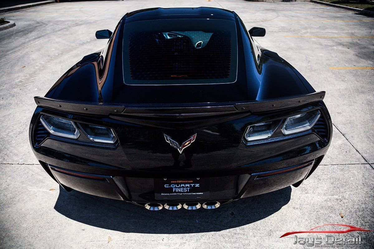 Black Corvette sports car, rear view, parked on concrete.