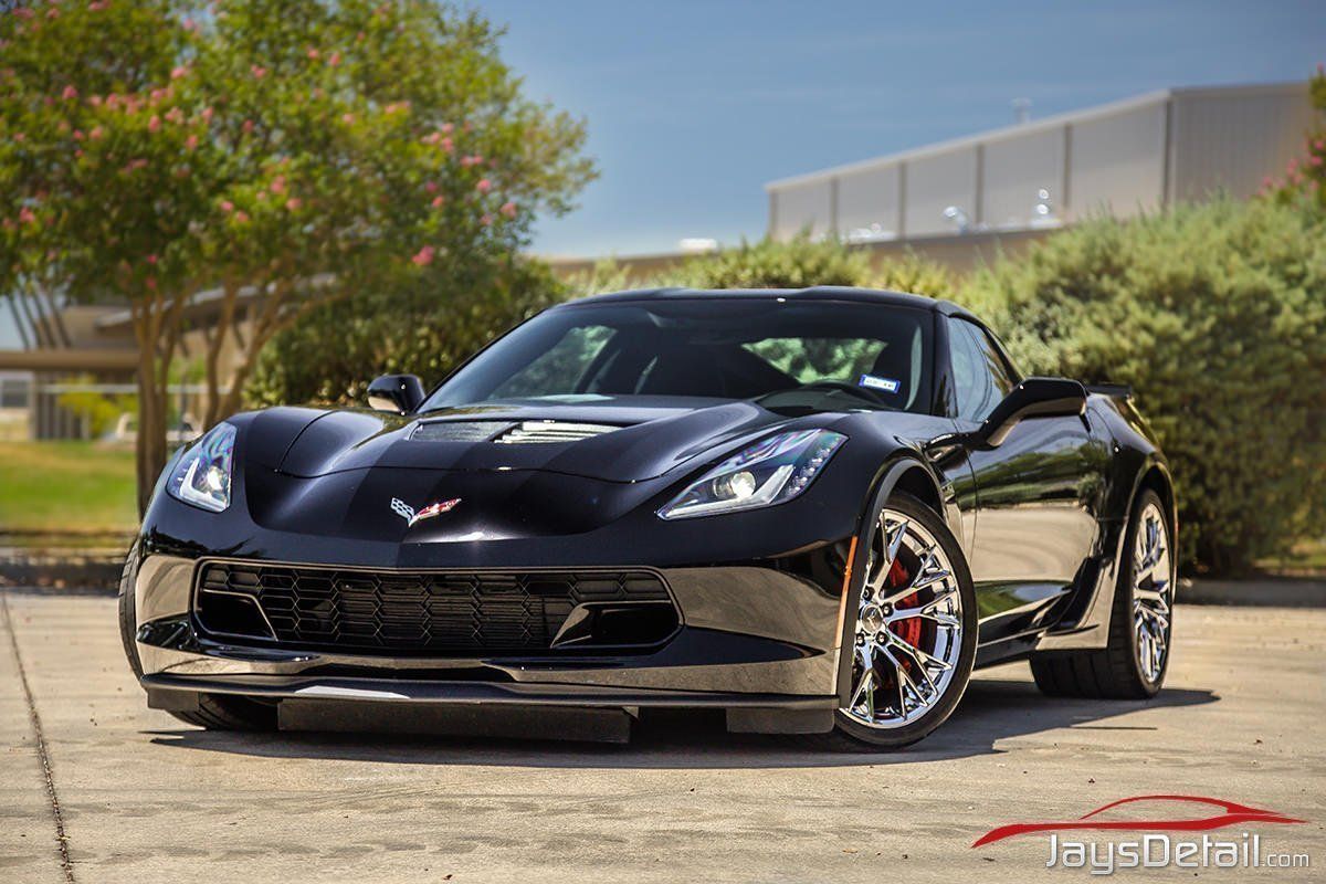 Black Chevrolet Corvette sports car parked on a paved surface, front view. Shiny chrome wheels and red brake calipers.