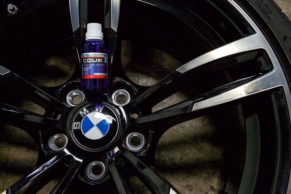 A bottle of car detailing product rests on a black and silver BMW wheel.
