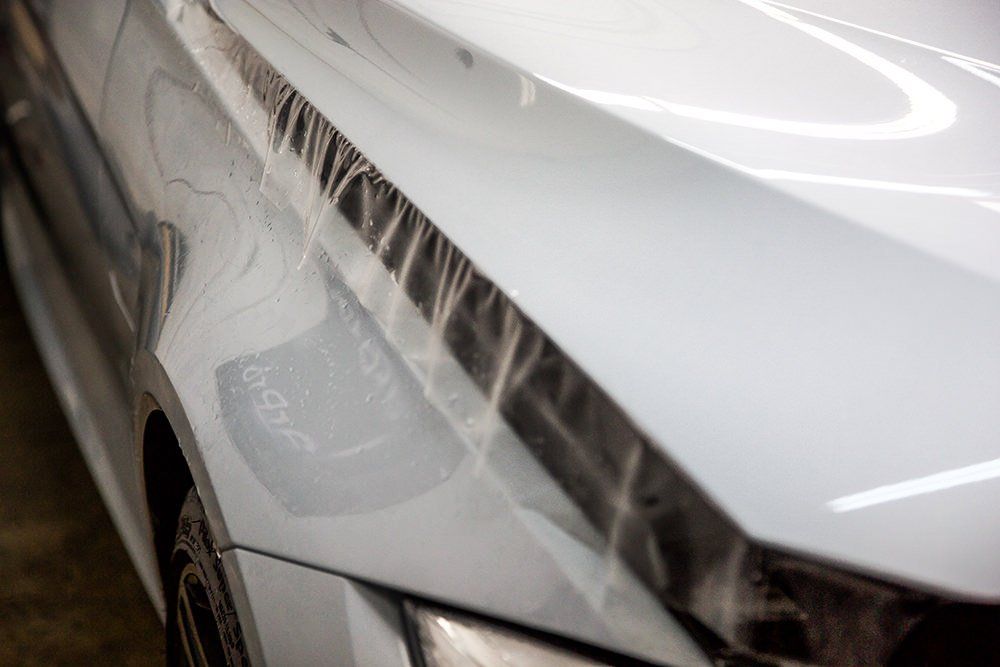 White car hood with black protective film being applied, close-up view.