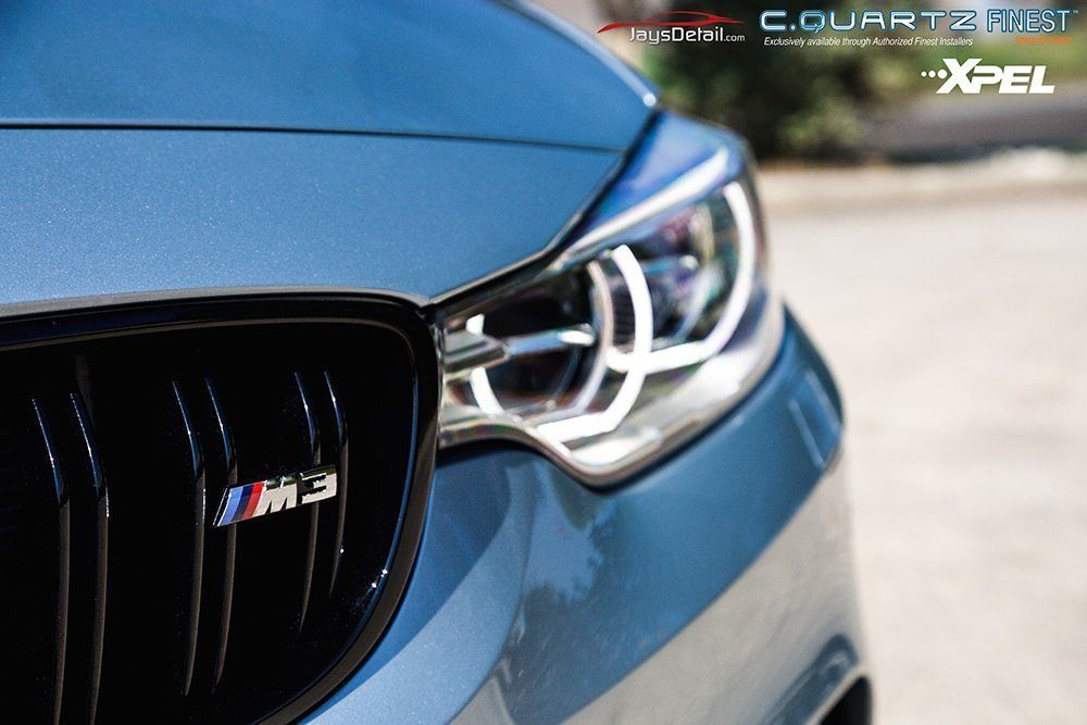 Close-up of a blue BMW M3 front end, showing the grille, headlights, and M3 badge.