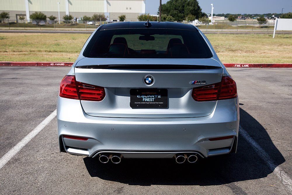 Silver BMW M3 sedan with black roof, parked in front of a building.