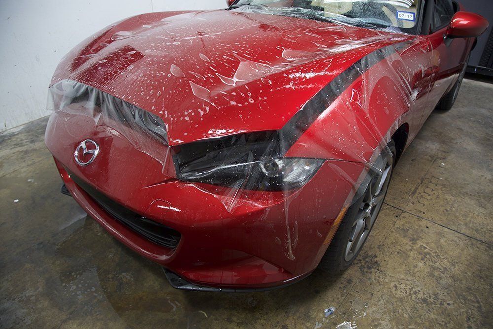 Red Mazda sports car with protective film applied to the hood.