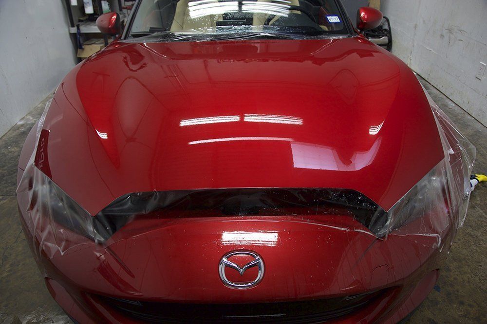 Red Mazda car with clear protective film on the hood and headlights, indoors.
