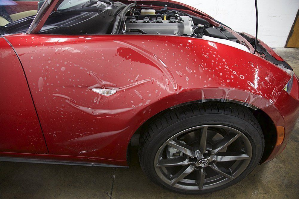 Red sports car with protective film applied to the front fender.